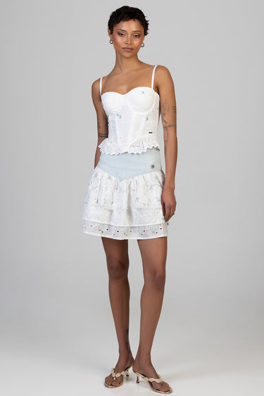 model wearing a white lace corset top with scalloped hem and a tiered lace skirt with a light blue waistband, beige sandals