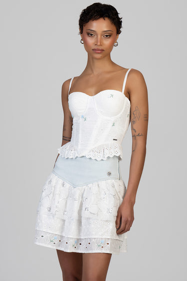 woman in a white embroidered peplum top with scalloped hem and a tiered eyelet skirt with light blue denim waistband