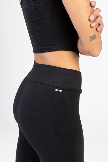 side view of a person wearing black knit denim pants with a high waist and a small metal brand tag on the back waistband