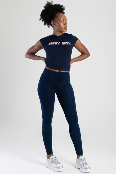 woman wearing dark indigo knit denim jeans and navy cropped t shirt with rhinestone lettering posing with hands on hips