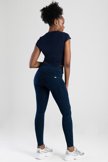 woman in dark indigo knit denim jeans and a navy cropped top, back view, white sneakers