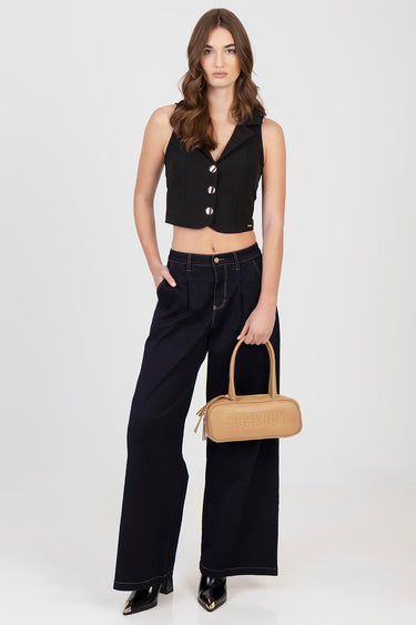 woman wearing black sleeveless cropped vest with large silver buttons, dark navy wide leg pants, holding tan handbag