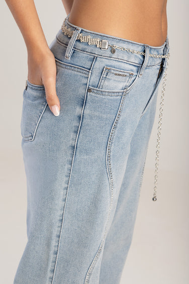 woman wearing light wash jeans with a silver chain belt featuring a square buckle and a heart charm, hand in pocket