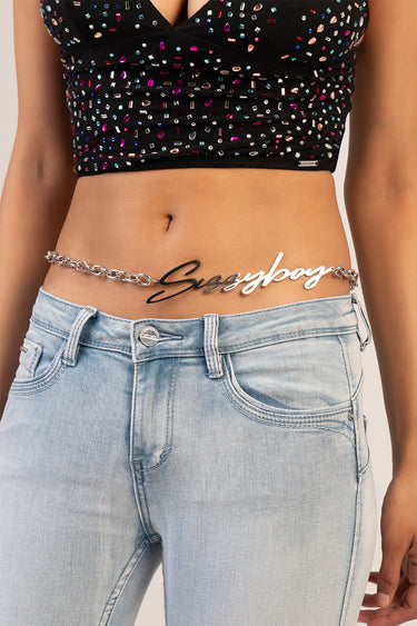 silver chain belt with a cursive name plaque worn at the waist over light wash jeans and a black studded crop top