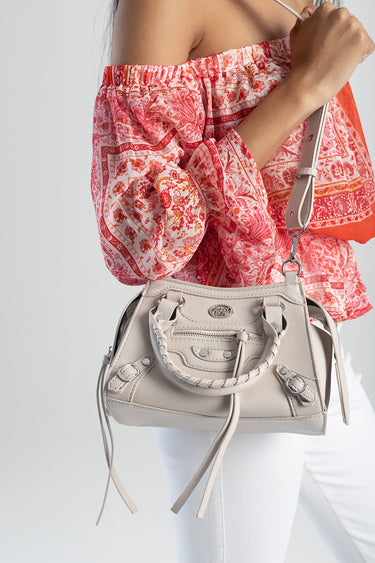 beige crossbody bag with braided handles and metal hardware against a pink floral off the shoulder top