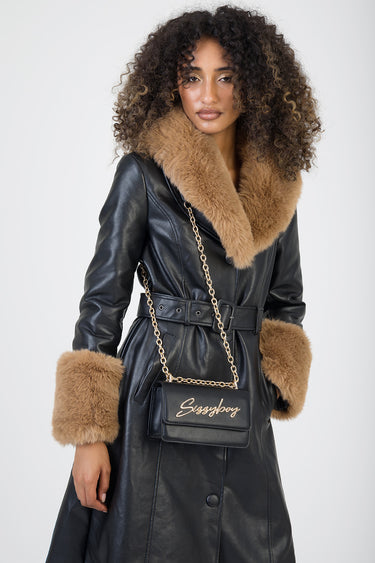 woman in black leather coat with tan fur collar and cuffs, carrying a black crossbody bag with a gold chain and script logo