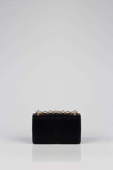 black rectangular crossbody bag with a gold chain strap on a white studio backdrop