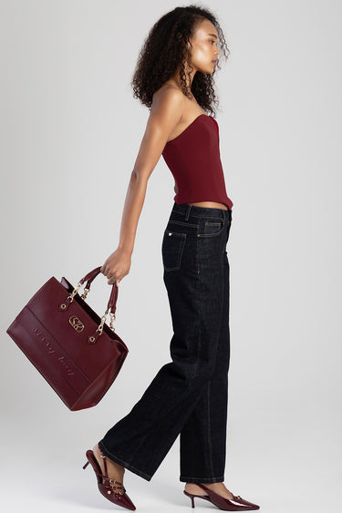 woman in a burgundy strapless top walks beside a dark wash jeans pair while holding a burgundy handbag with gold hardware