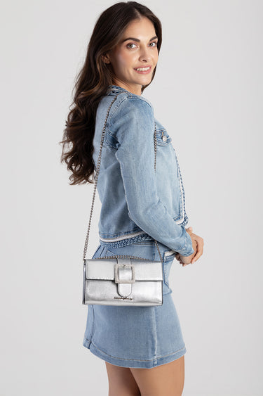 woman in light blue denim jacket with matching skirt carries a silver metallic chain bag