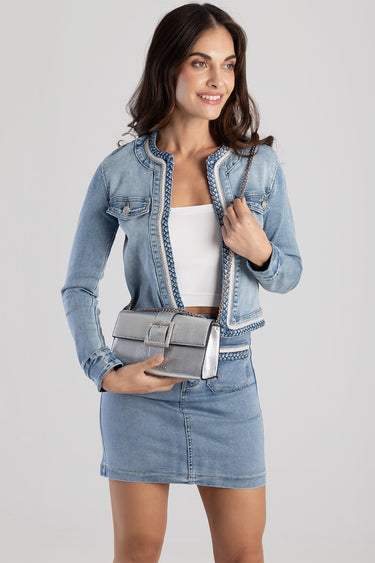 woman wearing a light blue denim jacket and matching denim skirt with braided trim, white top, holding a metallic silver