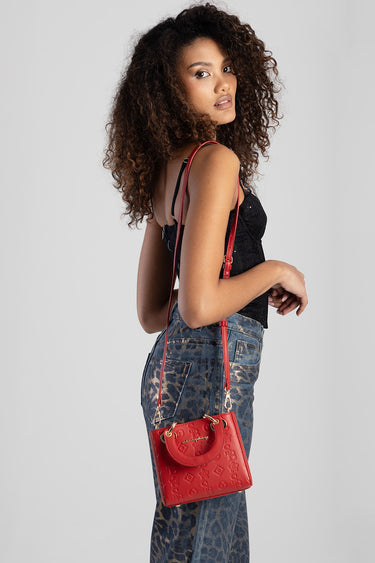woman with curly hair wearing a black sleeveless top and leopard print jeans carries a red embossed tote bag on a long strap