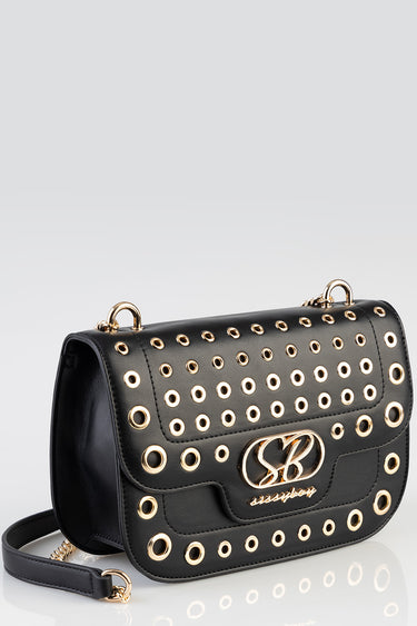 black leather crossbody bag with gold eyelets and a front logo emblem; brand Blue Jean Traders, adjustable strap.