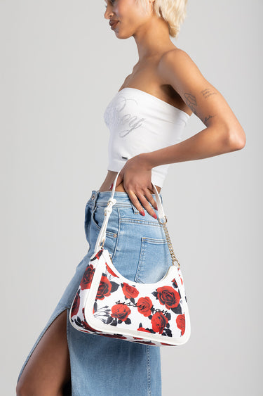 woman in a white tube top carries a white handbag with red rose print and chain strap