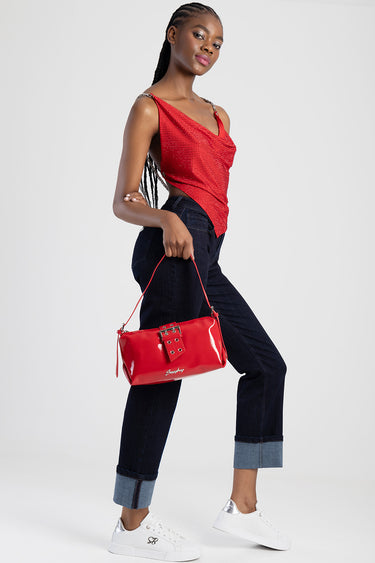 model wearing a red sequined top and dark cuffed jeans, holding a bright red glossy shoulder bag with a buckle