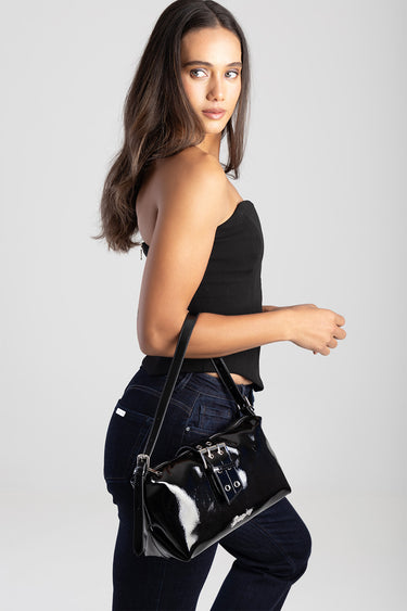 woman wearing a black strapless top and dark jeans carries a glossy black shoulder bag with buckles