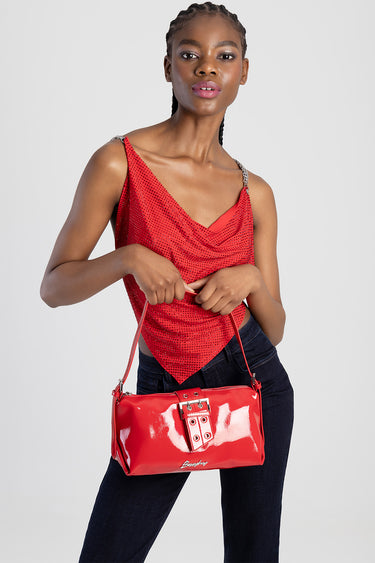 woman in a red sequined top carries a glossy red shoulder bag with a metal buckle.