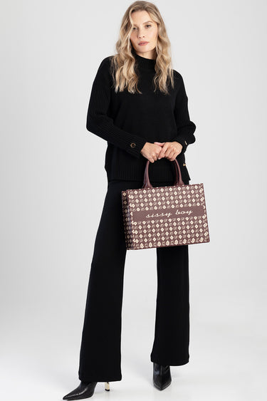 woman in black knit sweater and wide leg pants holds a brown patterned shopper bag with pink handles