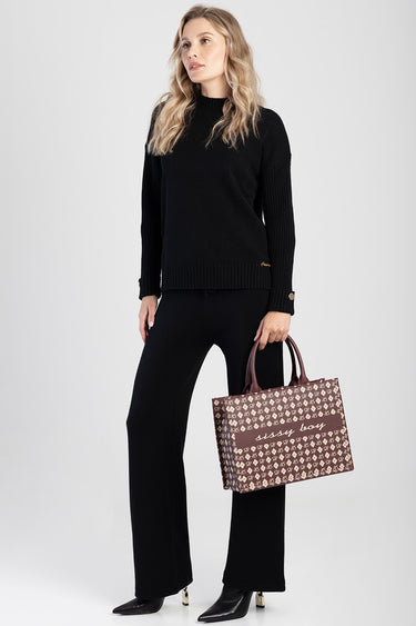 woman in a black knit top and wide leg pants holding a brown patterned shopper bag with two handles