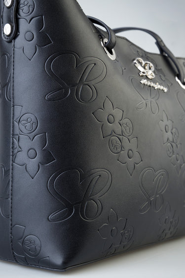 close up of a dark blue tote with embossed floral and heart patterns and metal logo hardware