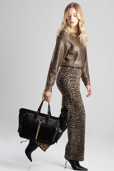 woman in a shimmering gold top and leopard print trousers carries a black handbag with gold hardware