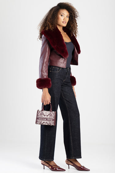 woman wearing a burgundy jacket with fur collar and cuffs, dark wide leg jeans, carrying a patterned burgundy handbag
