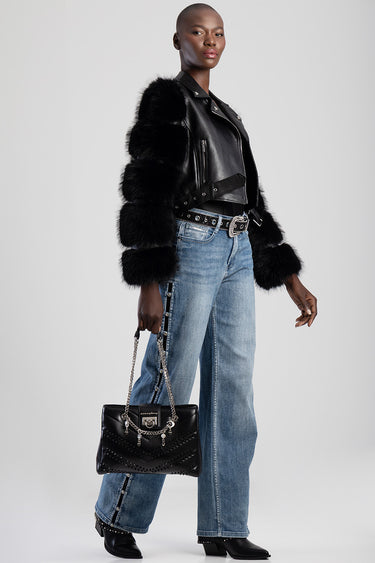 model in black fur coat over a leather jacket with blue jeans, carrying a black studded handbag with a silver chain strap