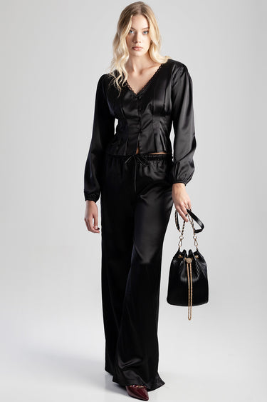 woman wearing a black satin blouse and matching wide leg pants, holding a black bucket bag with gold chain