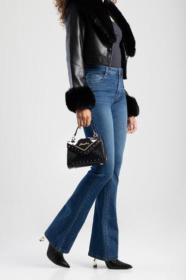 woman in black leather jacket with fur cuffs carries a small black studded crossbody bag with gold hardware