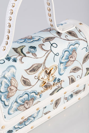 white mini bag by Blue Jean Traders with blue and brown floral embroidery, gold logo charm and studded white strap