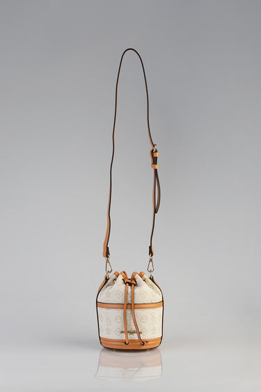 light beige bucket bag with tan leather trim, drawstring closure, long adjustable strap, gold hardware, logo print pattern