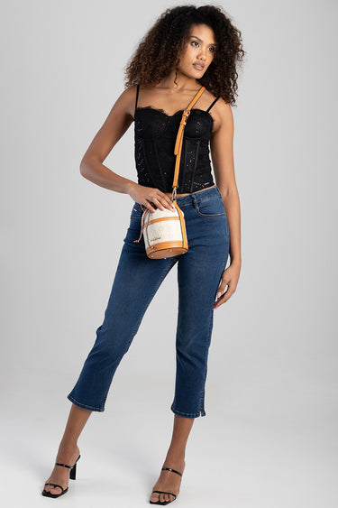 woman in black lace bustier top and blue jeans carries a tan and beige bucket bag with a strap