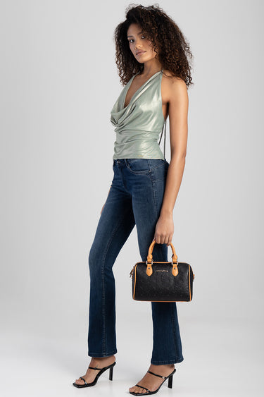 woman wearing blue jeans and a metallic sage top holding a black bowler bag with tan leather handles