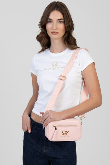 woman wearing a white t shirt carries a light pink crossbody bag with gold hardware and an adjustable strap