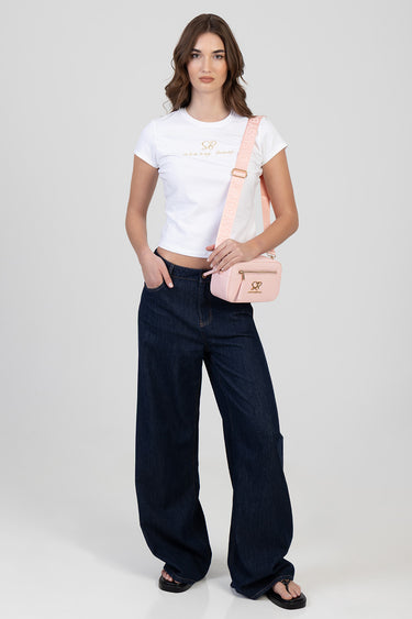 woman in a white t shirt and dark denim wide leg jeans carries a pale pink crossbody bag with a gold logo
