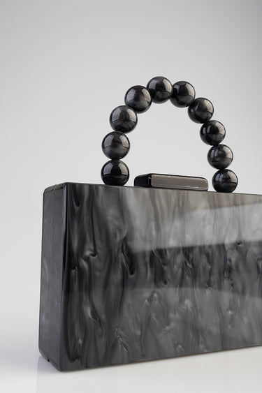 black glossy clutch bag with a round beaded handle against a light grey backdrop