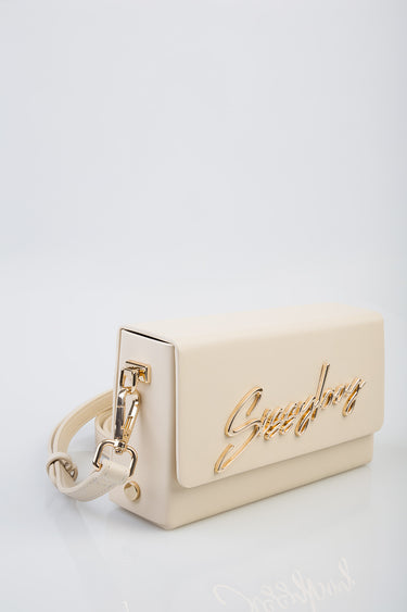 cream handbag with gold cursive logo and matching strap on a white surface
