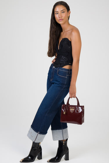 woman in a black lace strapless top and dark blue wide leg jeans, carrying a burgundy patent tote bag.