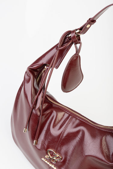 burgundy leather shoulder bag with gold hardware, zip top, and hanging luggage tag