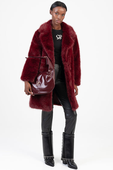 woman wearing a burgundy faux fur coat carries a burgundy glossy shoulder bag with a black top, black leather pants and