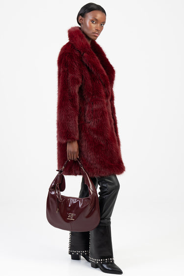 model wearing a burgundy fur coat carrying a burgundy hobo bag with a gold logo, black studded boots and leather pants