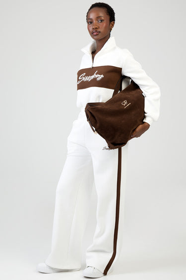 woman in a white and brown tracksuit holding a dark brown suede tote bag with a small logo