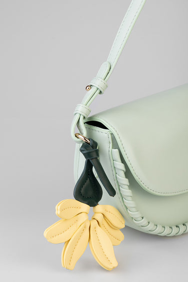 mint green shoulder bag with braided edges and a yellow flower charm on the strap