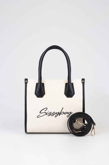beige canvas tote with black trim, two black handles, and a detachable black strap with gold hardware, front script logo