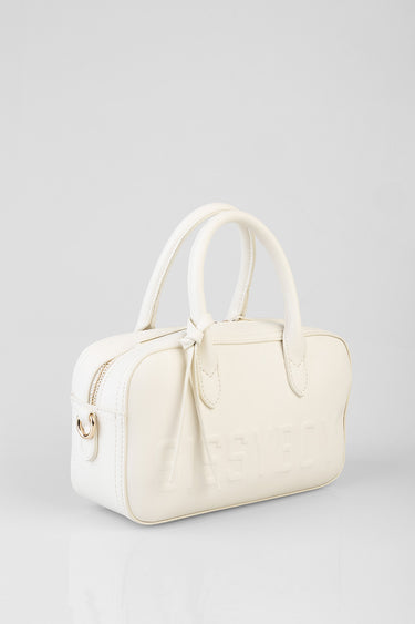 cream bowler bag with top zipper, knotted bow detail, two handles, embossed lettering on the side, and gold hardware