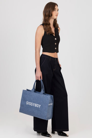 woman in a black sleeveless cropped top with silver buttons, wide leg dark denim pants, carrying a blue denim tote that