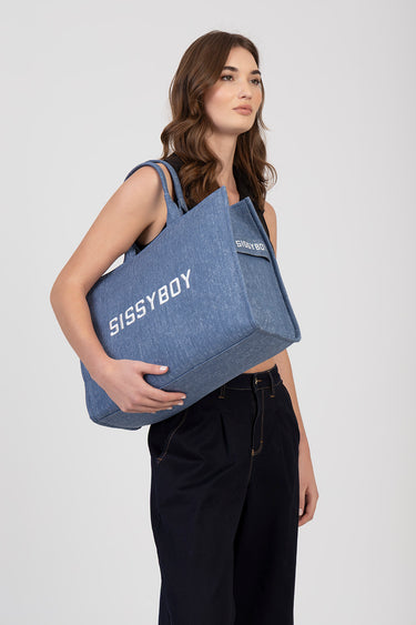 blue denim tote bag with white Sissyboy lettering, carried by a model in dark pants