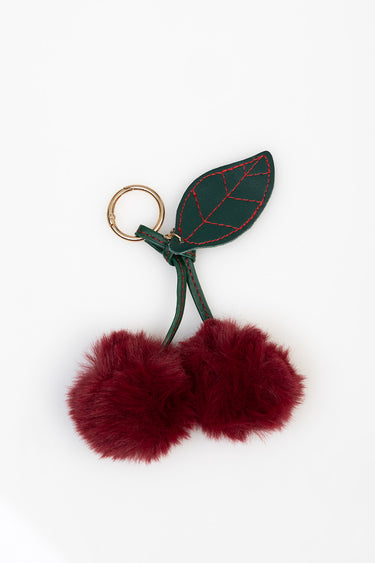 green leather leaf with red thread stitching attached to a gold key ring and two burgundy fluffy pom poms