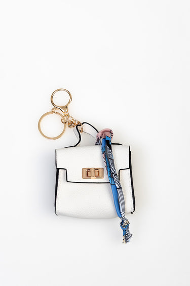 small white mini handbag charm with a gold clasp and black edging, with a blue scarf tied to a gold key ring