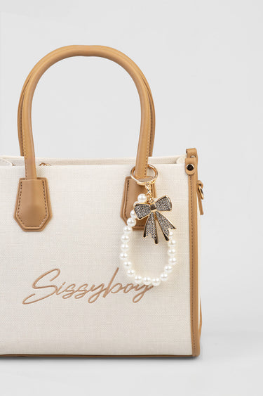 beige canvas handbag with tan handles and a pearl bead charm featuring a rhinestone bow