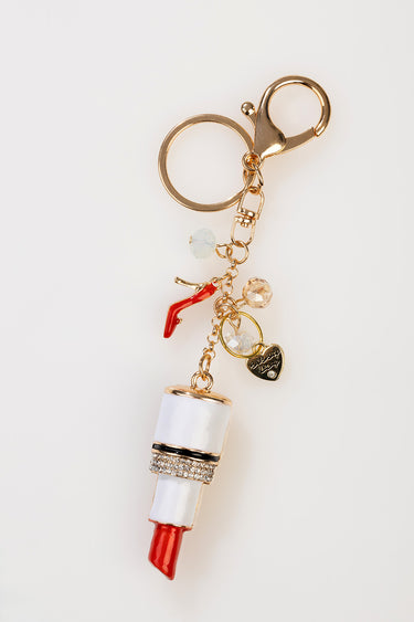 gold tone lipstick bag charm with a white band and rhinestone accent, dangling beads and a red lipstick pendant on a key